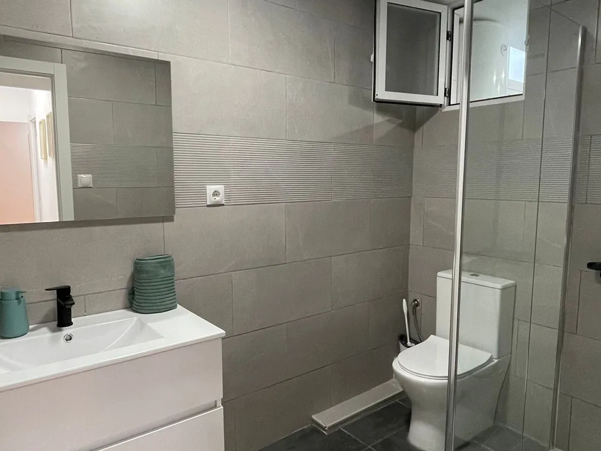 Baño reformado con ducha, mueble suspendido, grifería negra y azulejo gris